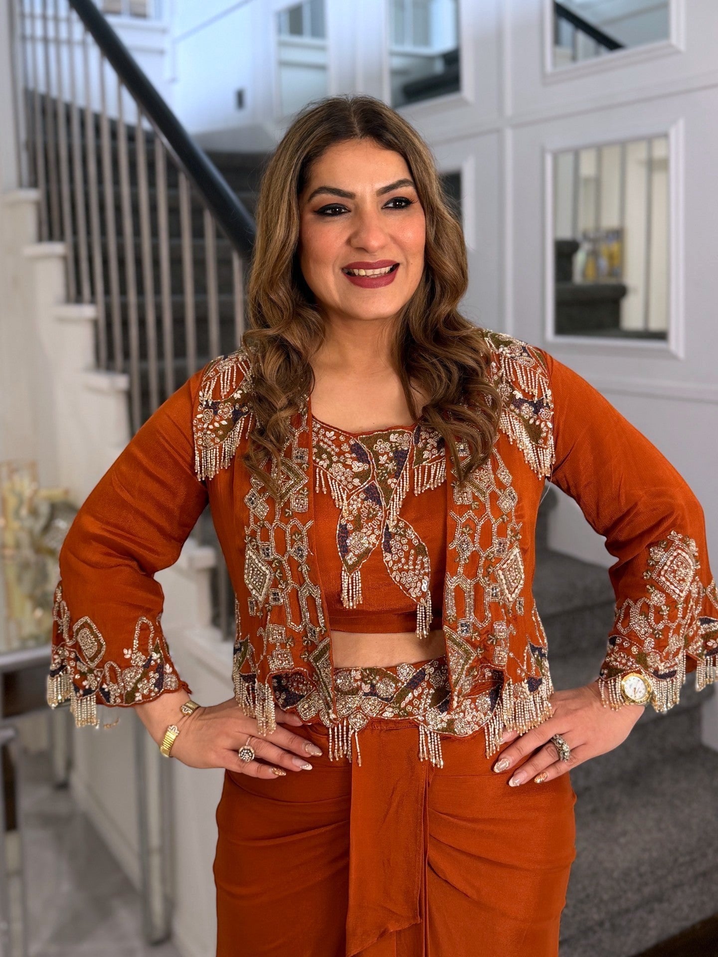 Woman wearing a rust-orange PanacheByDivya Indo-western outfit with intricate embroidery and beaded fringe details.